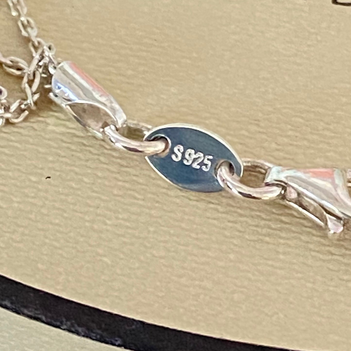 Close-up of a silver bracelet with '925' stamp on a beige background