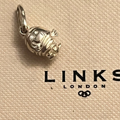 A sterling silver charm shaped like a small monkey wearing a striped shirt, resting on a textured beige Link's London brand card.