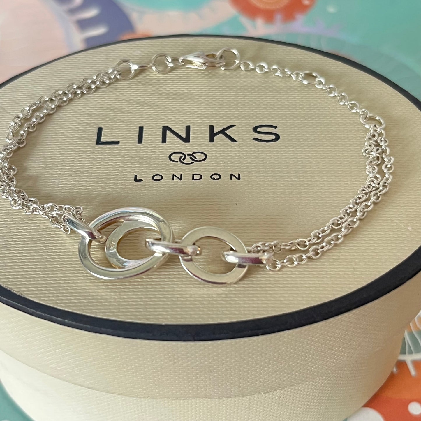 Links of London Sterling Silver interlocking rings resting on a double-strand chain bracelet
