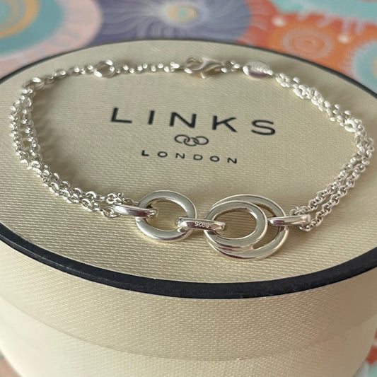 Links of London Sterling Silver interlocking rings resting on a double-strand chain bracelet