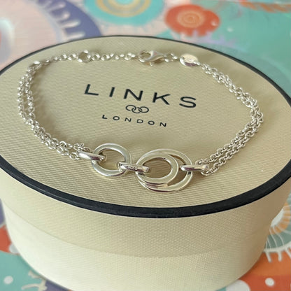 Links of London Sterling Silver interlocking rings resting on a double-strand chain bracelet