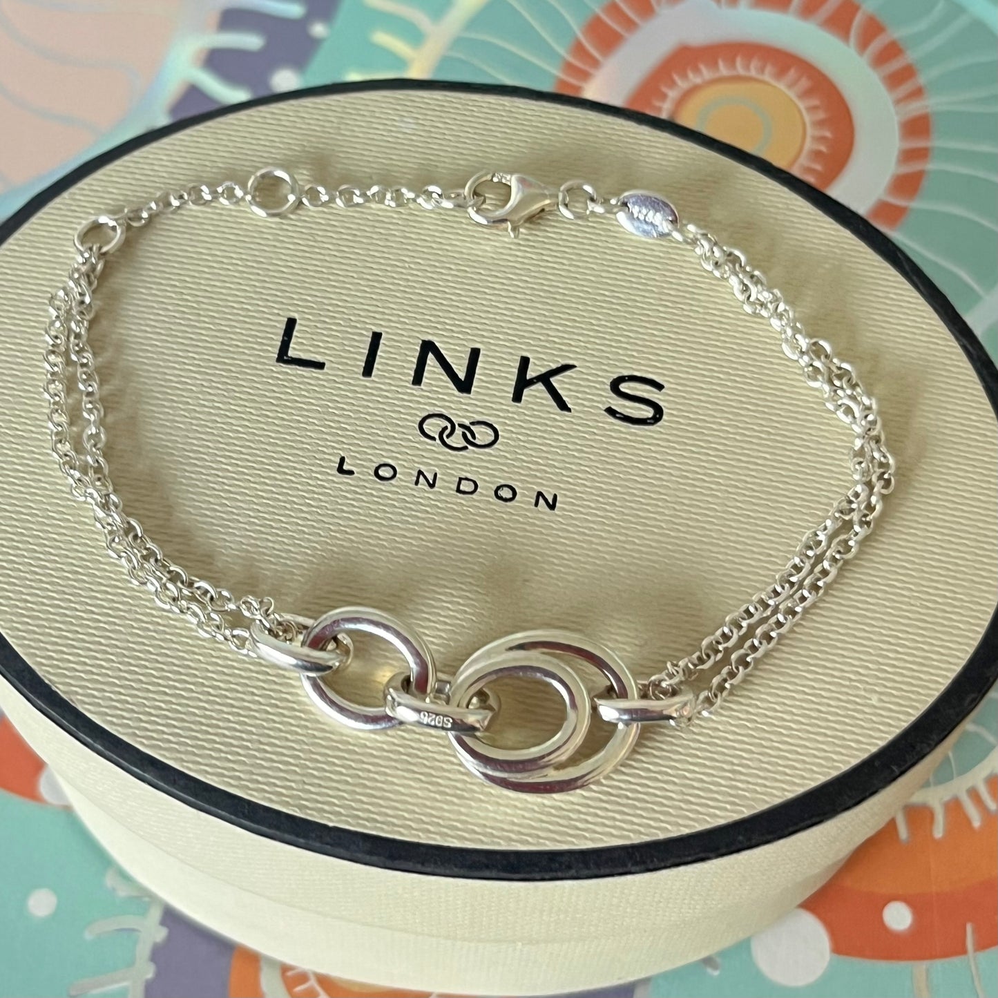 Links of London Sterling Silver interlocking rings resting on a double-strand chain bracelet