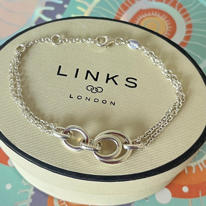 Links of London Sterling Silver interlocking rings resting on a double-strand chain bracelet