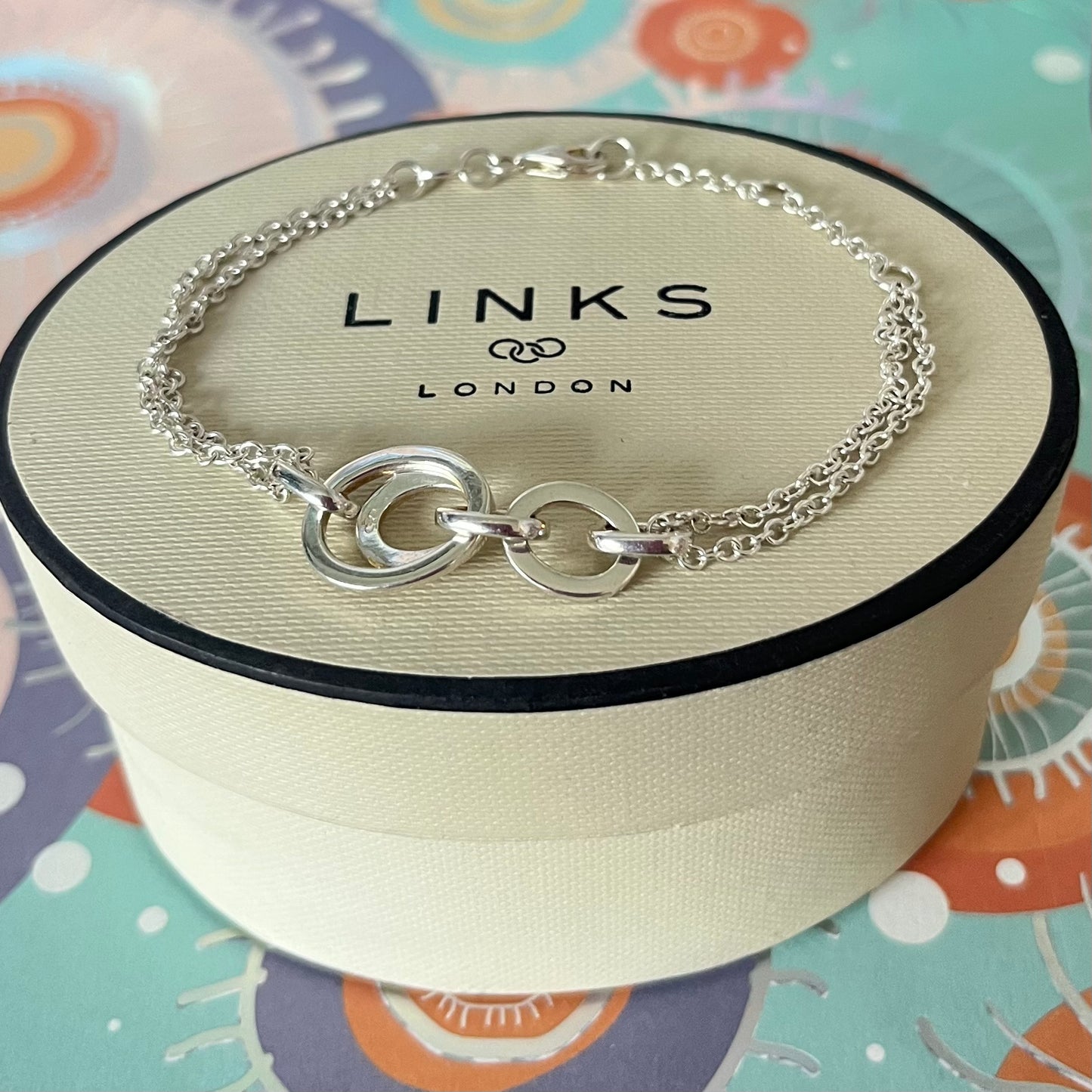 Links of London Sterling Silver interlocking rings resting on a double-strand chain bracelet