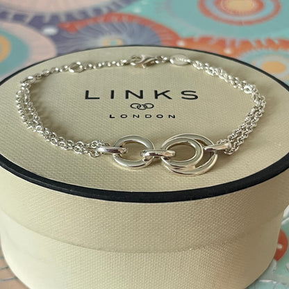Links of London Sterling Silver interlocking rings resting on a double-strand chain bracelet