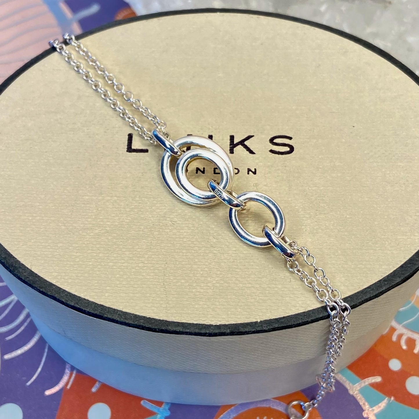 Links of London Sterling Silver interlocking rings resting on a double-strand chain bracelet