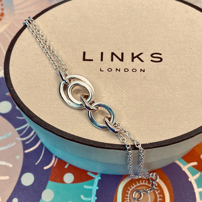 Links of London Sterling Silver interlocking rings resting on a double-strand chain bracelet