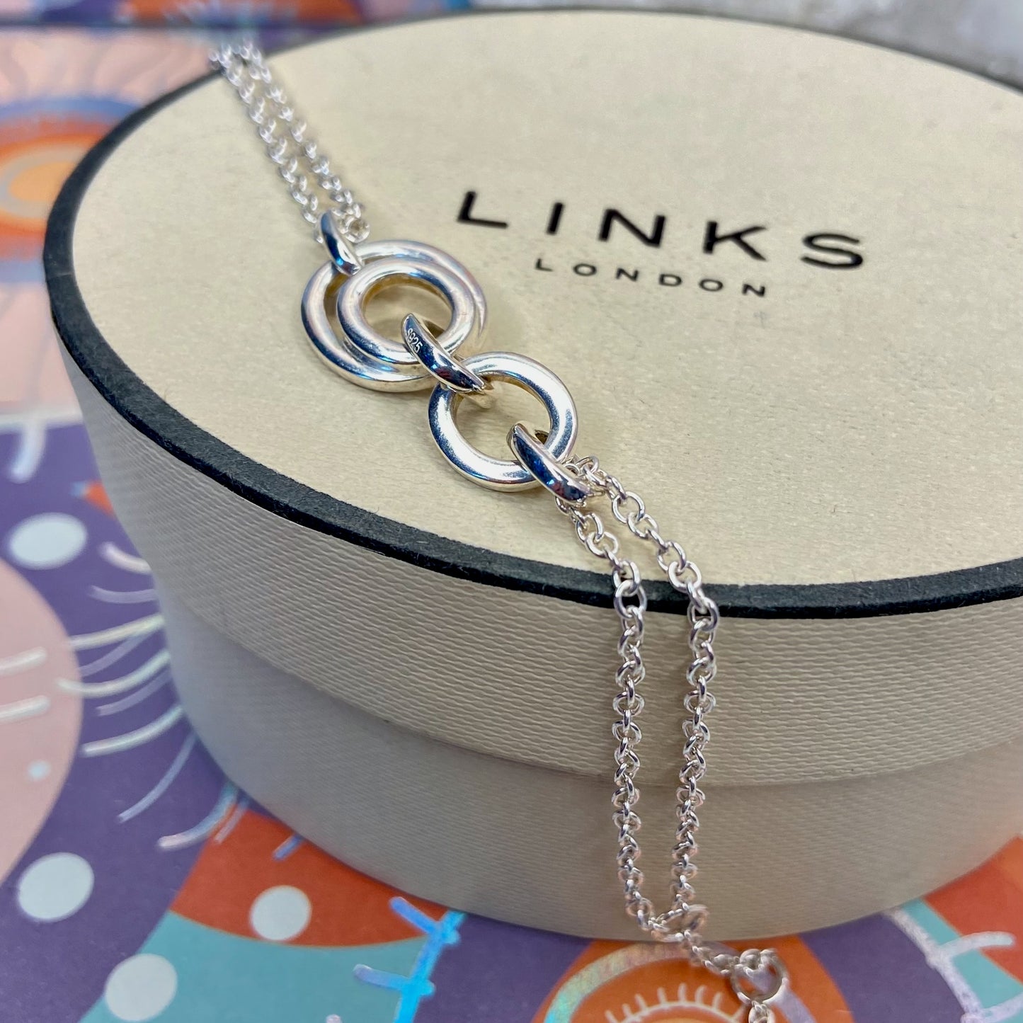 Links of London Sterling Silver interlocking rings resting on a double-strand chain bracelet